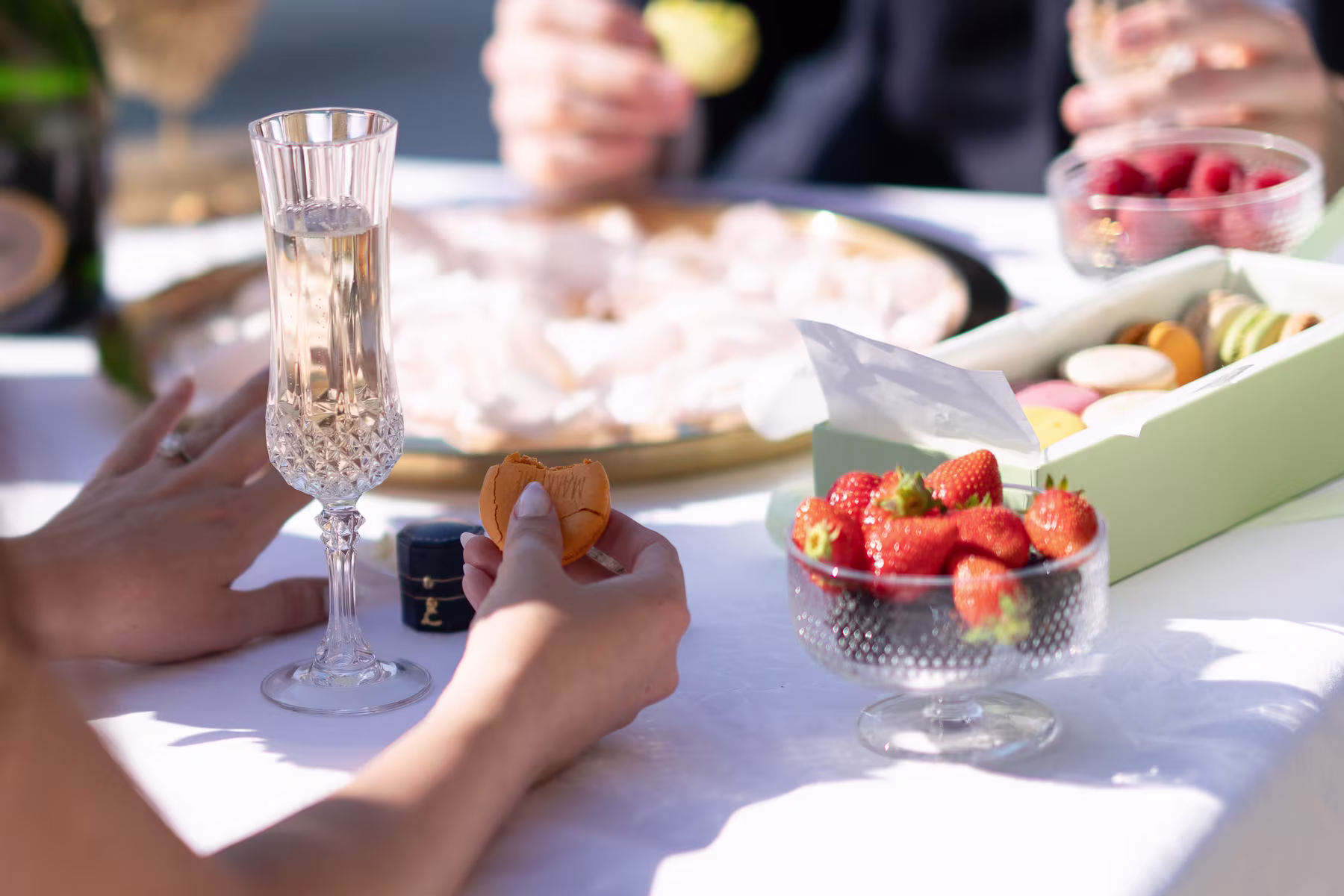 Champagne, macarons, and fresh strawberries on a white tablecloth during a private picnic proposal along the Seine in Paris