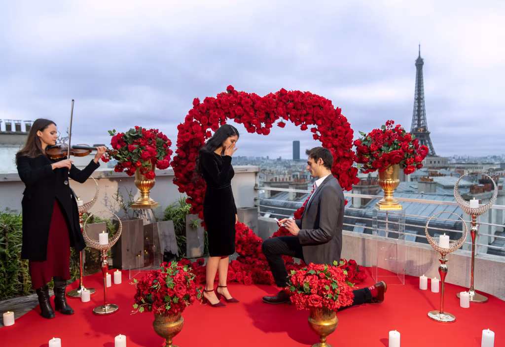 Residential Sablon rooftop proposal in Paris at sunset with big red love heart, red carpet, silk floral arrangements in Medici gold vases on clear pedestals, and flameless candles overlooking the lit Eiffel Tower