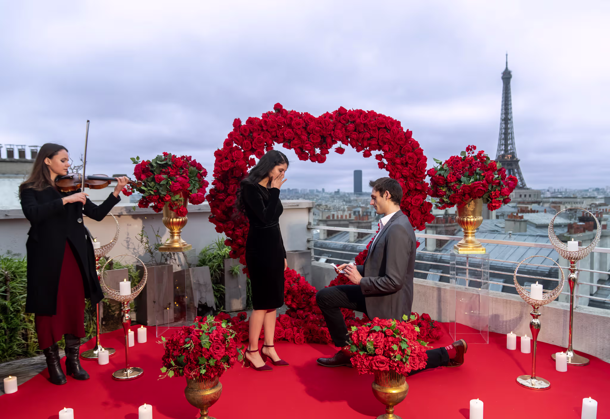 Residential Sablon rooftop proposal in Paris at sunset with big red love heart, red carpet, silk floral arrangements in Medici gold vases on clear pedestals, and flameless candles overlooking the lit Eiffel Tower