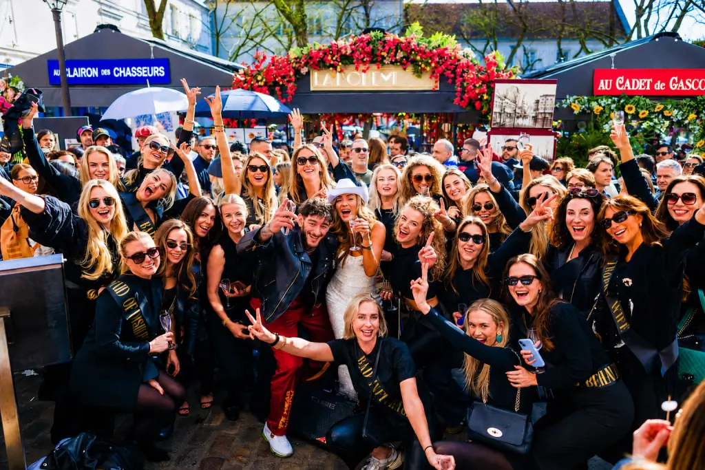 Large bachelorette party group in matching black outfits and sashes celebrating with champagne in Montmartre Paris